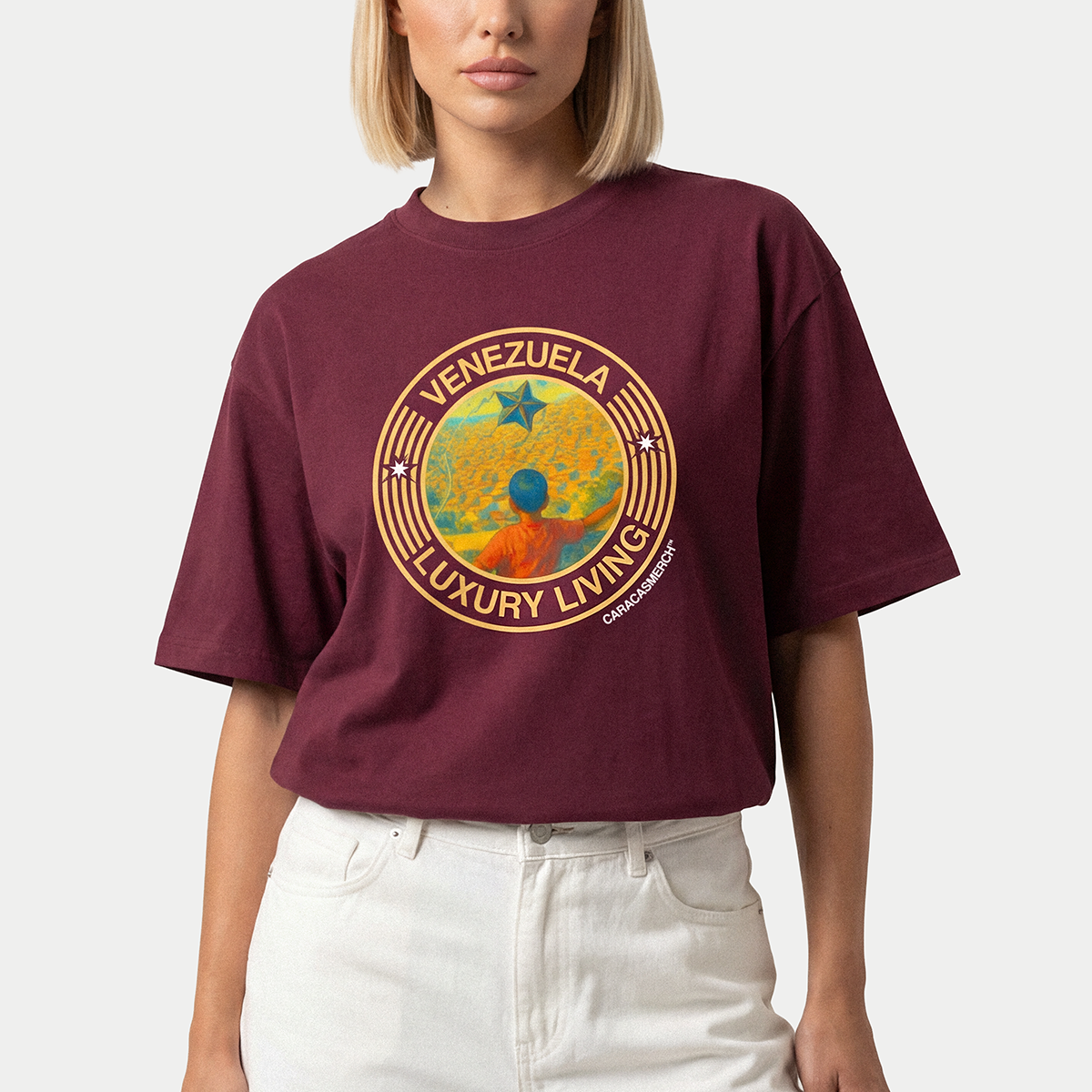 Mujer llevando la camiseta burdeos «Venezuela Luxury Living» de Caracas Merch con un gráfico circular de sol y estrella en el pecho